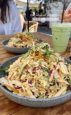 two bowls filled with food sitting on top of a wooden table next to a drink