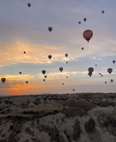 many hot air balloons are flying in the sky above some rocks and sand at sunset