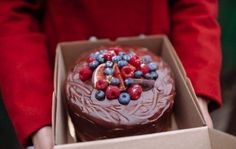 a chocolate cake with berries and blueberries on top in a box, being held by someone