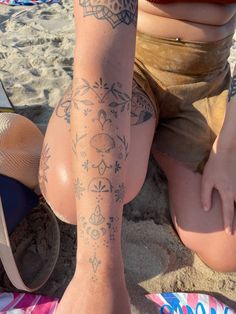 a person sitting on the beach with tattoos on their legs