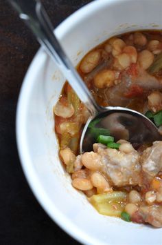 a white bowl filled with beans and meat next to a spoon on top of a table