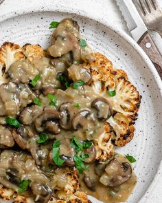 a white plate topped with cauliflower covered in gravy next to a fork