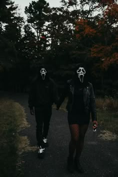 two people wearing masks walking down a path in the woods with their hands held by each other