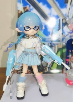 a doll with blue hair and glasses is standing on a white table in front of a glass display case