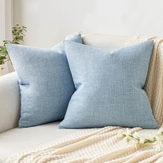 two blue pillows sitting on top of a white couch next to a potted plant