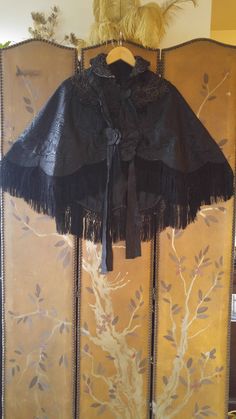 "One of a kind amazing Victorian black brocade embroidered fringed cape! This awesome cape has embroidered collars and across shoulders and front, the embroidery is a light black/ brown colour. There is a large black ribbon band that comes around the back of neck and down front sides with ribbon flowers at the ends and ties up the front, the ribbon is torn in places, could be easily replaced if you have a good seamstress! The black crochet and fringing is amazing! There are metal hook and eye fa Black Evening Cape, Black Fall Festival Cape, Black Cape For Fall Festivals, Traditional Black Cape For Fall, Black Cape For Costume Party, Black Bohemian Cape For Festivals, Elegant Black Cape For Costume, Bohemian Black Cape For Festival, Black Capelet For Costume