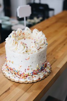 a white frosted cake with sprinkles sitting on top of a wooden table