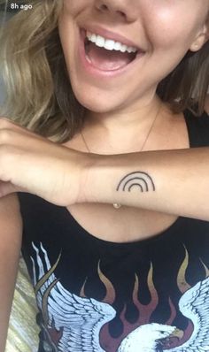 a woman with a tattoo on her arm smiling at the camera and holding onto her wrist