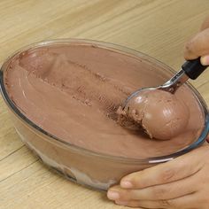 a person scooping chocolate into a bowl on a wooden table with a spoon in it