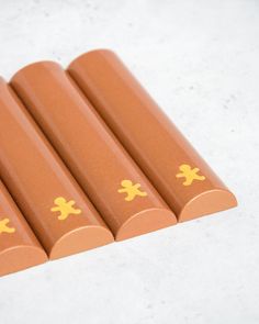 four brown crayons with yellow stickers are lined up on a white surface