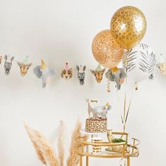 an animal themed birthday party with gold balloons and animals on the wall above it is a cake