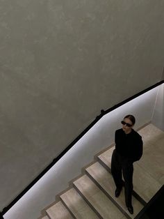 a woman is walking down the stairs in a black suit and sunglasses with her hand on her hip