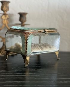 an old glass box sitting on top of a wooden table next to candlesticks