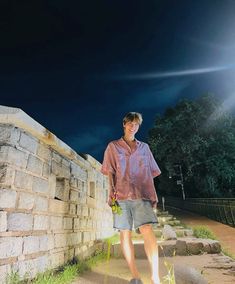 a man standing next to a stone wall at night with the sun shining on him