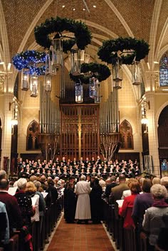 a large group of people standing in front of a church organ with wreaths hanging from the ceiling