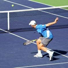 a man in blue shirt and grey shorts playing tennis on court with ball coming towards him