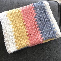 a crocheted blanket is laying on top of a couch with the colors of blue, yellow, and pink