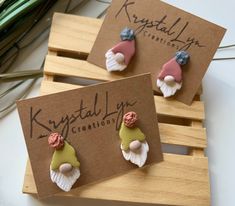 two small earrings are sitting on top of a wooden box, one is pink and the other is green