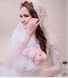 a woman wearing a wedding dress and veil holding a bouquet of flowers in front of her face