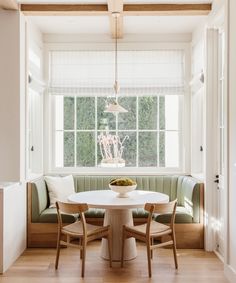 a white table and chairs in front of a window next to a bench with pillows on it