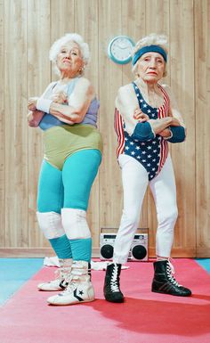 two older women standing on top of a red carpet in front of a wooden wall