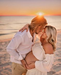 a pregnant couple kissing on the beach at sunset