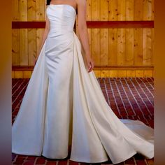 a woman in a white wedding dress standing on a brick floor next to a wooden wall