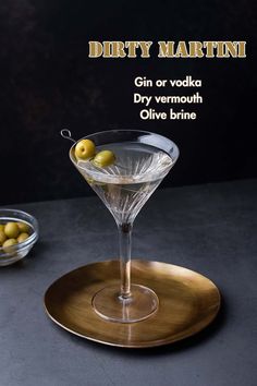 a martini glass with olives in it on a gold serving platter next to a bowl of olives