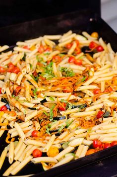 a pan filled with pasta and vegetables on top of a stove burner covered in seasoning