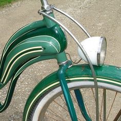 an old fashioned green bicycle parked on the side of a dirt road with grass in the background