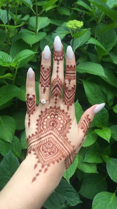 a hand with henna painted on it in front of some green plants and leaves