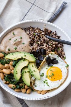 a white bowl filled with beans, avocado, and an egg on top