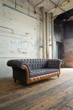 an old couch sitting on top of a hard wood floor next to a brick wall