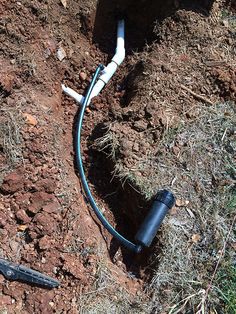 a hose connected to a pipe laying on the ground next to some grass and dirt