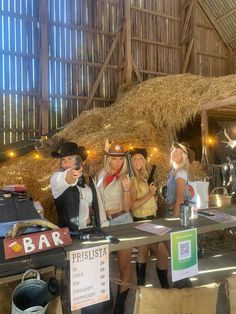 three women in cowboy hats are standing behind a table with drinks and food on it