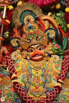 an elaborately decorated mask is displayed in front of a wall with flowers and other decorations