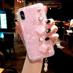 a woman's hand holding up a pink phone case with pearls and bows on it