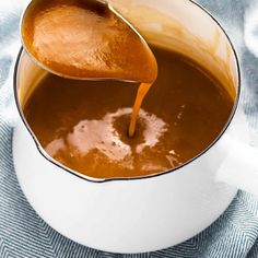 a spoon is pouring caramel sauce into a white bowl on a blue and white towel