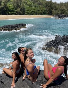 four women in bikinis sitting on rocks near the ocean