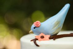 a small blue bird sitting on top of a white cake covered in frosting and flowers