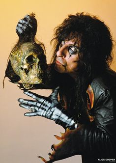 a man with long hair and makeup holding a skull in one hand while wearing gloves