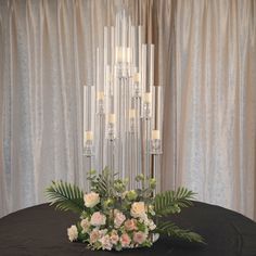 a centerpiece with candles and flowers on a table in front of curtained backdrop