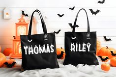 two black bags with white letters on them sitting in front of pumpkins and bats