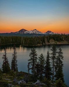 the sun is setting over a lake with trees and mountains in the backgroud