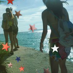 two girls standing on the edge of a cliff looking out at the water and stars in the sky