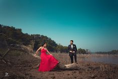 a man and woman in formal wear standing next to a tree trunk on the beach