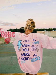 a woman wearing a pink sweatshirt with writing on it and her arms spread out in the air