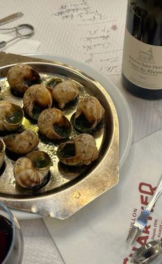 a silver plate topped with clams next to a bottle of wine