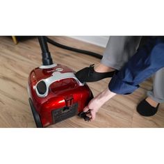 a person vacuuming the floor with a red and white hoover bagged vacuum cleaner