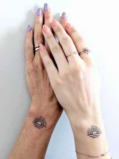 two hands holding each other with small tattoos on their wrists and fingers, both showing the sun